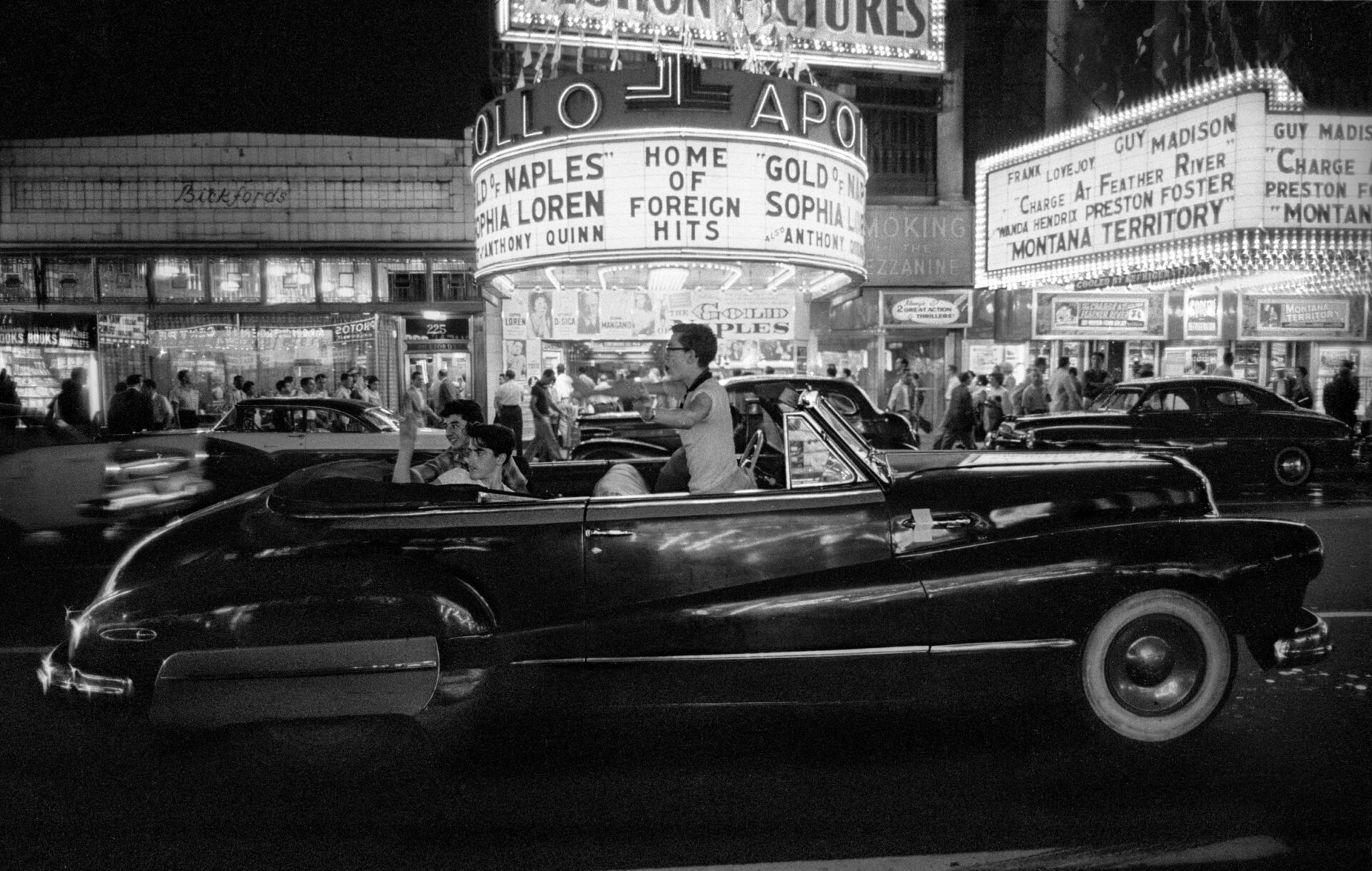 Teenagers cruising in a convertible through Times Square at night in New York City in 1957. The Apollo Theater marquee is in the background.
