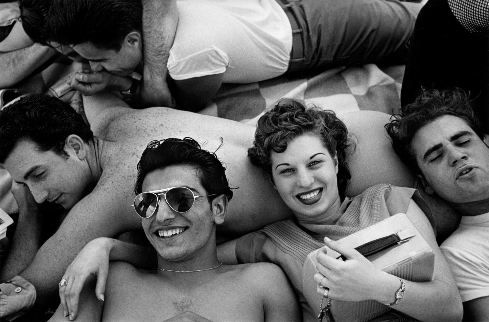 Five happy teenagers lying together on the sand with a transitor radio in 1949